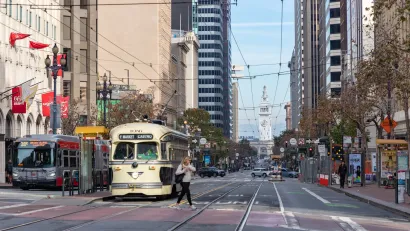 Streetcar and bus stopped at station on Market Street in San Francisco with Ferry Building visible in background.