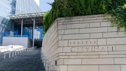 Close-up of engraved stone Seattle City Hall sign in front of wide steps leading to modern glass building.
