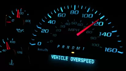 Close-up of car speedometer showing 120 mph speed with digitally displayed ' VEHICLE OVERSPEED' warning