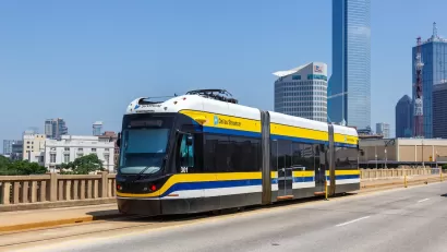 White and yellow DART streetcar on bridge in Dallas, Texas with skyscrapers in background.