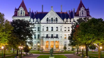 New York state capitol building with green lawn and statue in front at dusk.