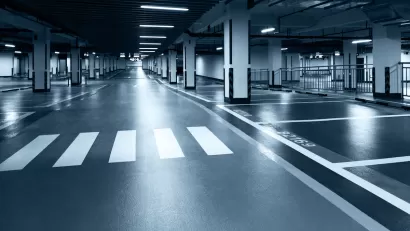 Black and white tinted photo of underground parking garage with black floor, white crosswalk, and harsh lighting.