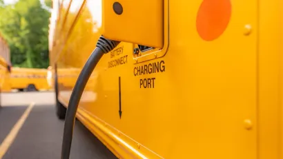 Close-up of open charging port with charging cable plugged in on yellow electric school bus.