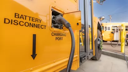 Close-up of charging port on yellow electric school bus plugged in at charging station.