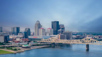 Louisville, Kentucky skyline with river and bridge in foreground at dusk.