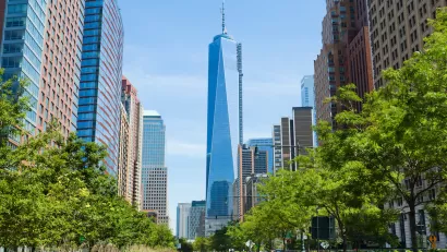 View of One World Trade Center down straight street with bright green trees on either side.