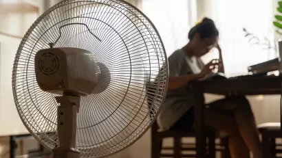 Close-up of floor fan operating with blurred woman sitting at table in background.