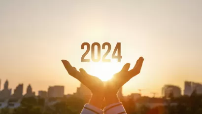 Graphic of person's hands with 2024 in middle against backdrop of city skyline and golden hour sky with rays coming through.