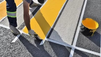 Close-up of man painting white and yellow crosswalk on asphalt.