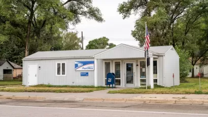 Small rural USPS post office in manufactured one-story grey building with American flag in front.