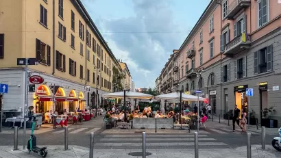 Pedestrianized street in Milan, Italy with outdoor dining tables and umbrellas.