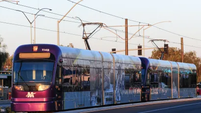 Purple Phoenix light rail train connected to overhead wires at sunset.