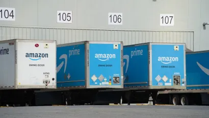 Blue and white Amazon trucks parked at loading docks at warehouse.