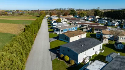 Aerial view of mobile home community in rural area with homes lined up diagonally next to small road.