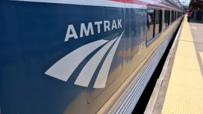 Close-up of Amtrak logo on blue passenger train stopped at outdoor station platform.