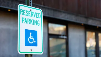 Close-up on white sign with green "Reserved Parking" letters and blue accessibility symbol.