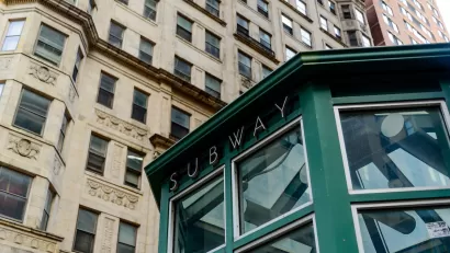 Green subway station entrance kiosk with brick buildings in background.
