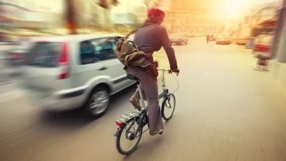 Cyclist on folding bike riding next to silver car on city street.