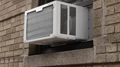 Close-up of white air conditioning window unit in window of brown brick building.