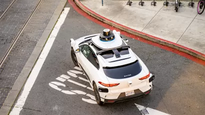 Overhead view of white Waymo self-driving car in San Francisco, California with shared bikes and scooters visible on adjacent sidewalk.