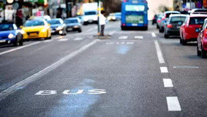 Close-up of white BUS letters on asphalt bus lane with blurred bus and traffic in background.