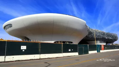 Amorphous white building for Lucas Museum of Narrative Art in Los Angeles, California under construction behind green construction fence.
