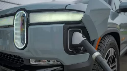 Close-up of front corner of grey Rivian truck with charger plugged in.