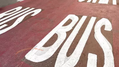 White BUS ONLY letters on red painted bus lane on street.