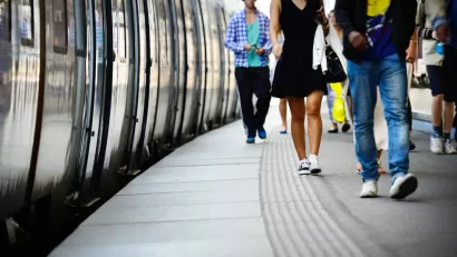 Low shot of side of subway or commuter train and passengers walking on platform next to it.