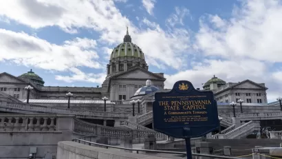 View of Pennsylvania state capitol building with historical plaque in foreground.