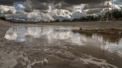 Low view of Glendale Narrows section of Los Angeles River with concrete bottom and cloudy storm sky over head.
