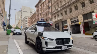 White Waymo self-driving taxi on street in San Francisco, California with brick buildings in background.