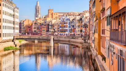 Old residential buildings along canal with ornate church in background in Girona, Catalonia, Spain.
