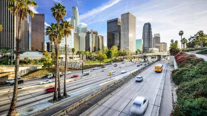View of traffic on freeway with Los Angeles skyline and palm trees in background