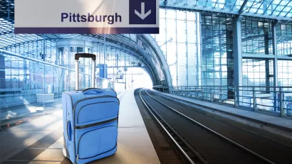 Blue suitcase sits on empty train platform with sign above labeled "Pittsburgh."