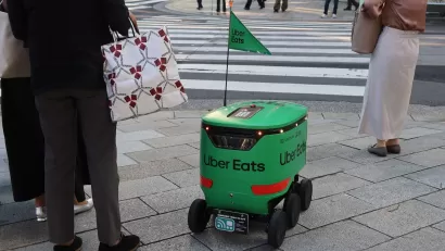 Green Uber Eats delivery robot waits at crosswalk in Tokyo, Japan.