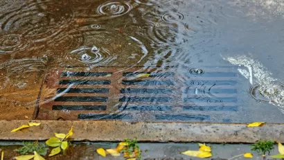 A leaf-free rusty street drain covered in a few inches of water.