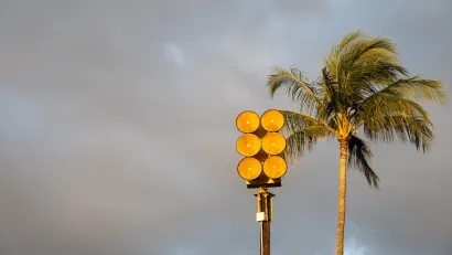 Tsunami sirens installed on top of pole in front of tall palm tree in golden stormy sky in Maui, Hawaii.