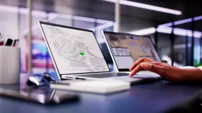 Close-up of laptop with GIS parcel map open and hand resting on keyboard in modern office.