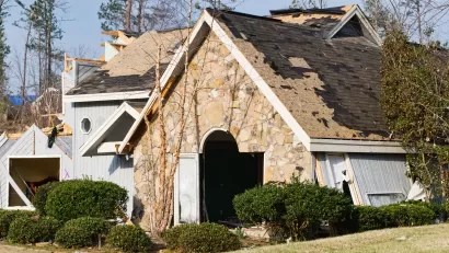 Front view of stone home with severe tornado damage and portions of roof ripped off.