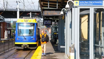 Outdoor train platform for light rail train in Minneapolis, Minnesota with passenger walking toward blue and yellow train.