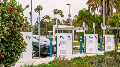 Cars parked and plugged in at an EV charging lot in Santa Monica, California surrounded by palm trees.