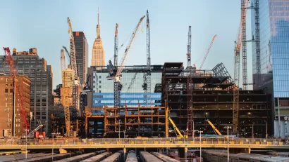 Construction site and cranes in New York City with Empire State Building visible in background.