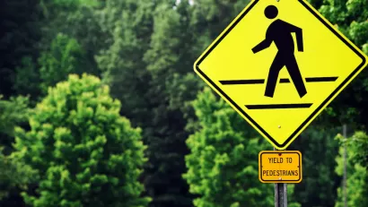 Yellow 'Yield to pedestrians' sign with graphic sign of person walking across street.