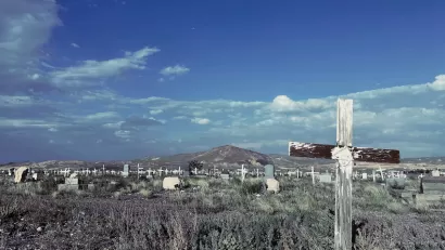 Old cemetery with weathered wooden cross grave markers in Goldfield, Nevada with mountain in background and blue sky.