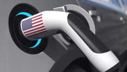 An electric vehicle charger with an American flag sticker is shown plugged into a car.