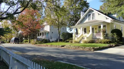 Large historic homes and white picket fences line a street.