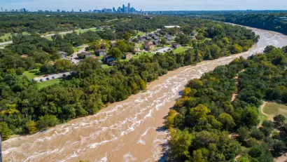 The Colorado River is flooded with brown water with the skyline of Austin, Texas in the background.