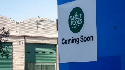 Austin, TA sign reading "Whole Foods Coming Soon" adorns a blue wall across the street from warehouses.