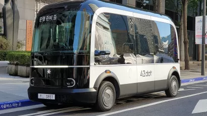 A small boxy driverless shuttle pulled up to a curb.